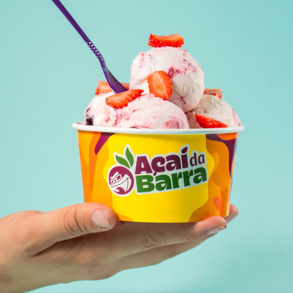 Menina sorridente segurando casquinha de sorvete, em ambiente iluminado pelo sol.